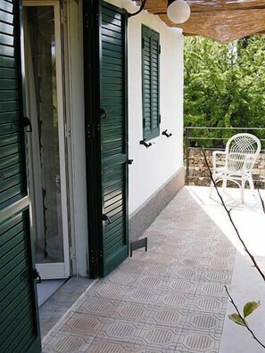 A covered outdoor area with a patterned floor, a white chair, and a door with green shutters.