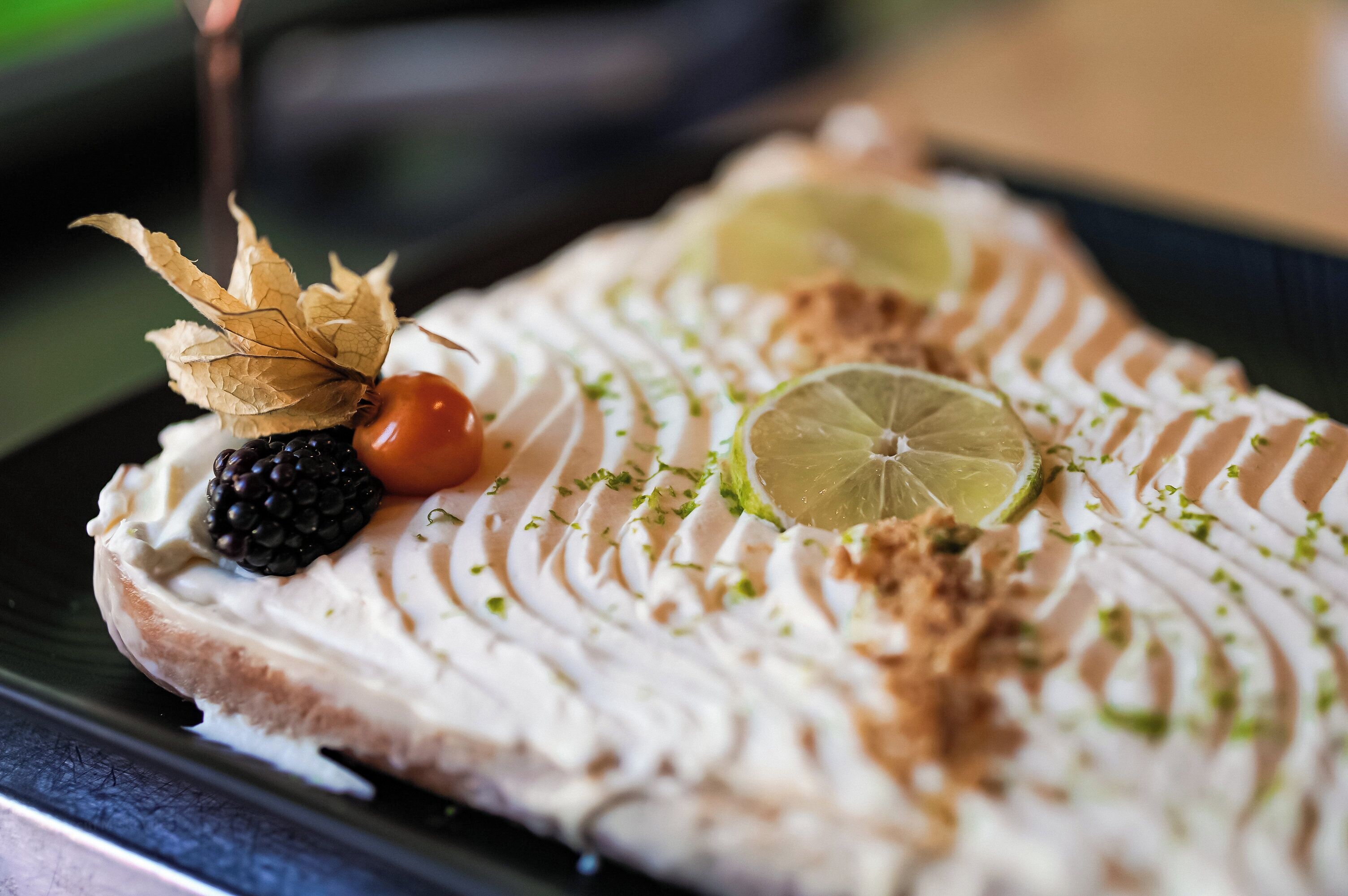 A dessert with whipped cream, blackberries, and lime slices on a plate.