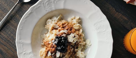 Desayuno con avena, tostadas, jamón, un gofre y una taza de café sobre una mesa de madera.