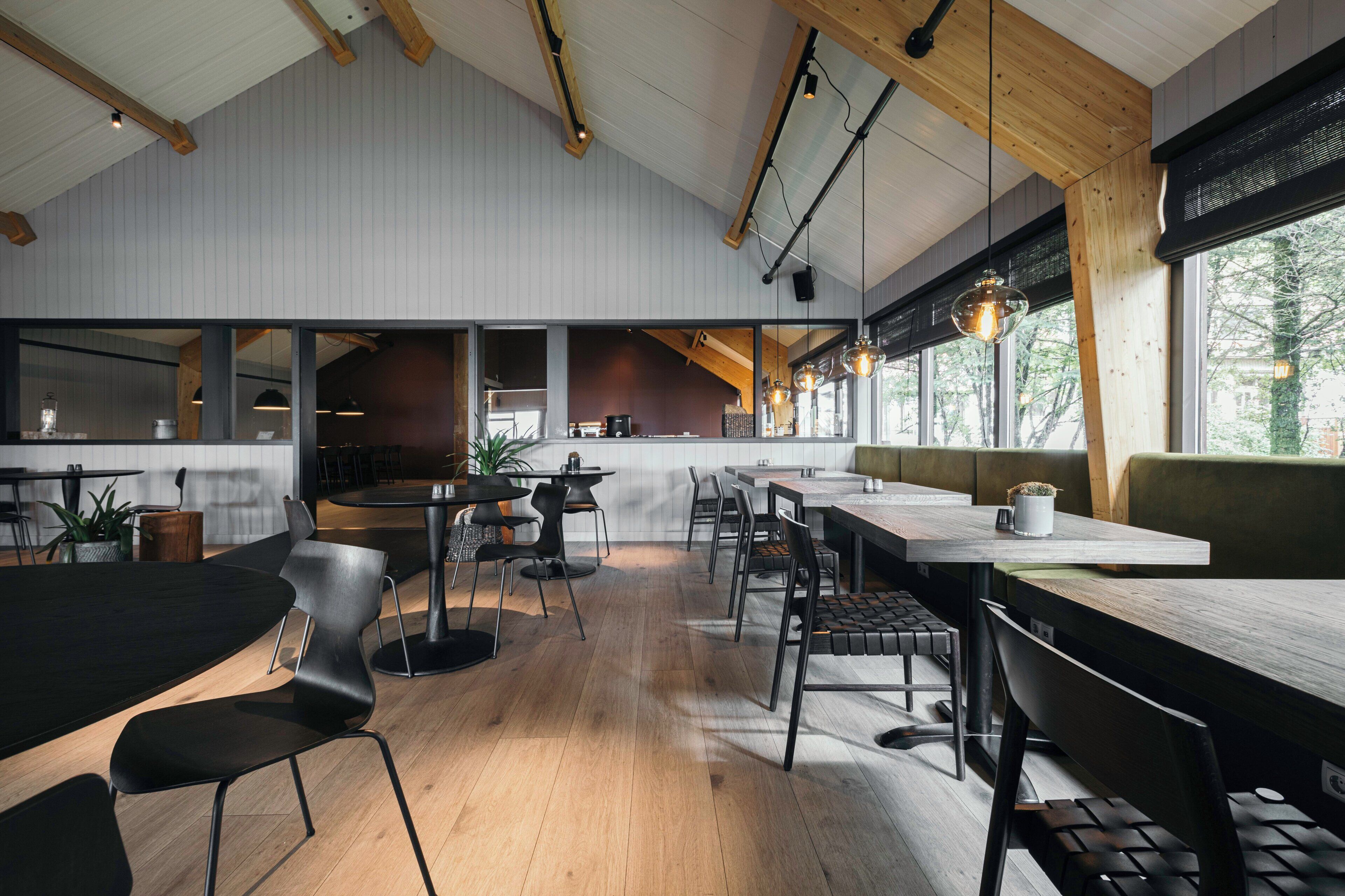 A modern dining area with wooden beams, black chairs, and tables.