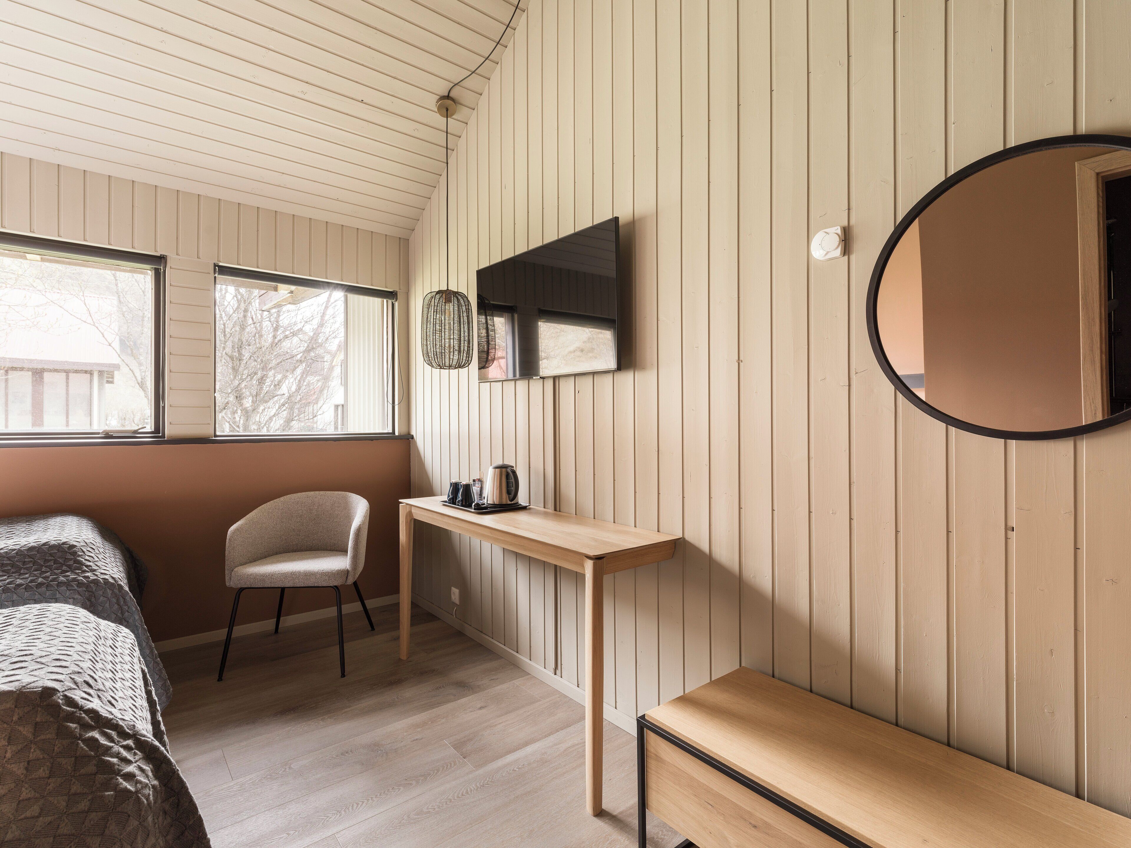 A room with a bed, a chair, a small table, a TV, and a mirror.