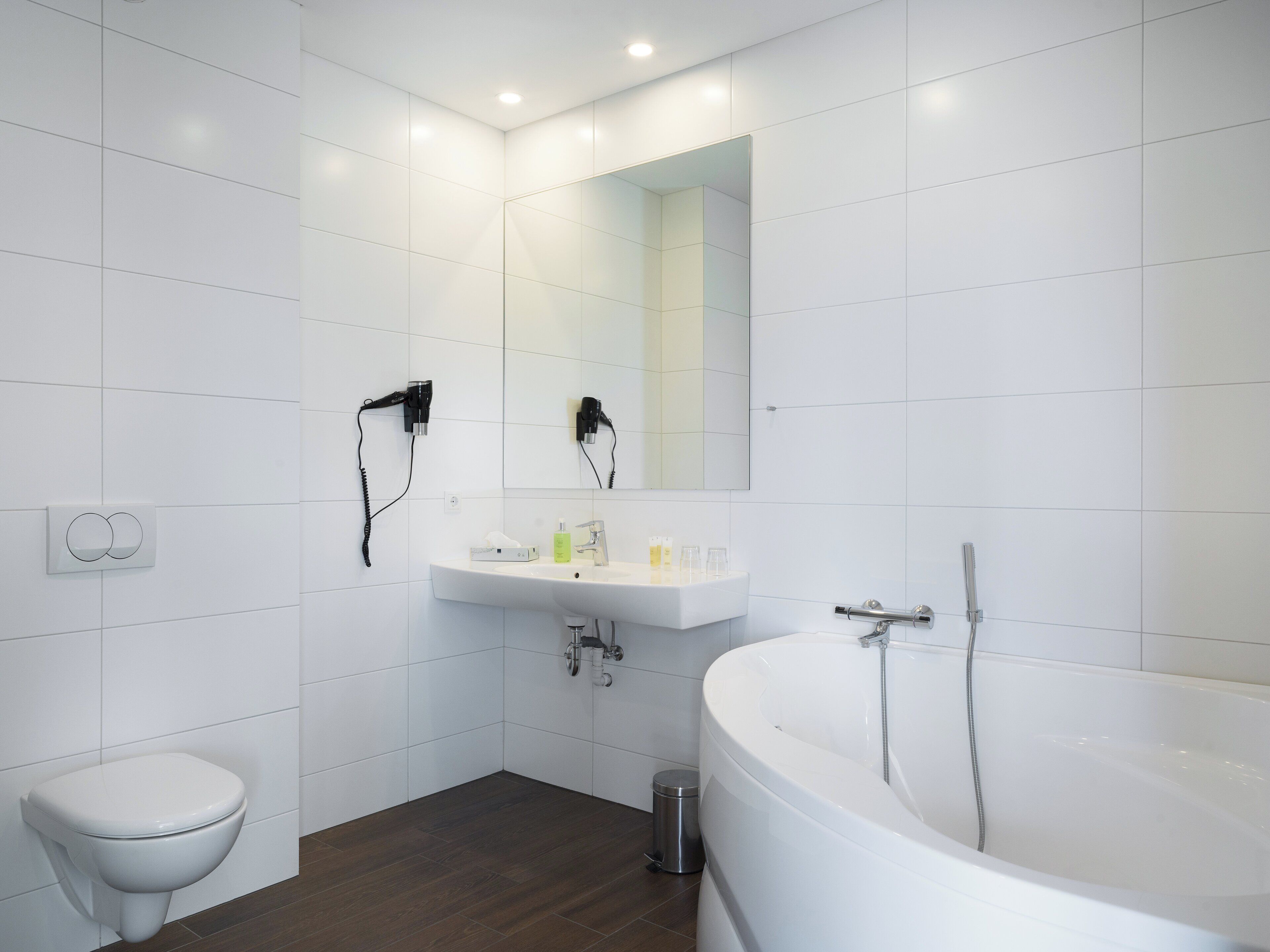 Uma casa de banho moderna com lavatório branco, espelho e banheira.