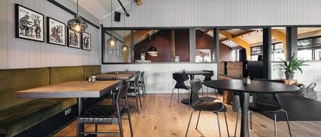 Un comedor moderno con mesas y sillas de madera, techo alto con vigas a la vista y obras de arte enmarcadas en las paredes.