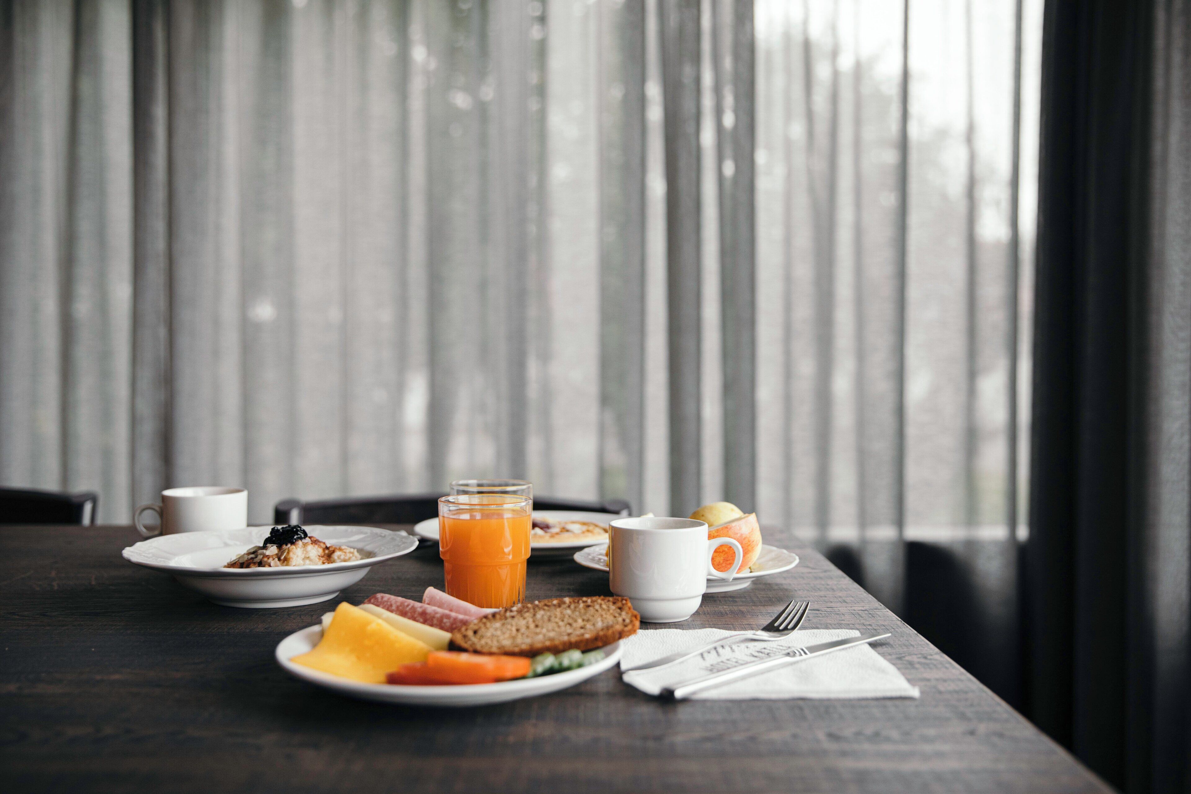 Una mesa de desayuno con platos de comida, un vaso de jugo de naranja y una taza de café.