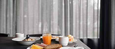 Una mesa de desayuno con platos de comida, un vaso de jugo de naranja y una taza de café.