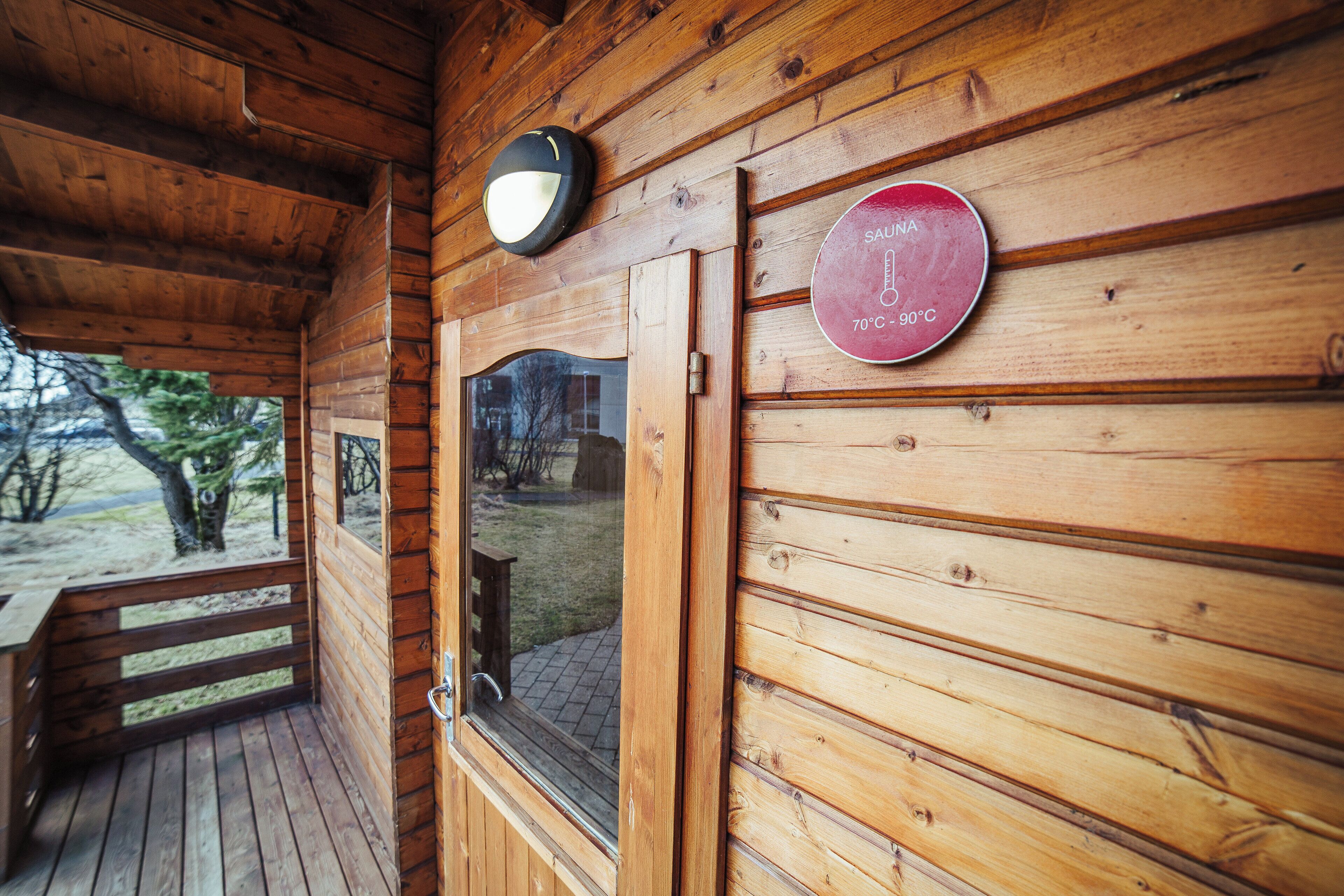 Een houten chalet met een glazen deur, een houten terras en een temperatuuraanduiding van 70°C tot 90°C.
