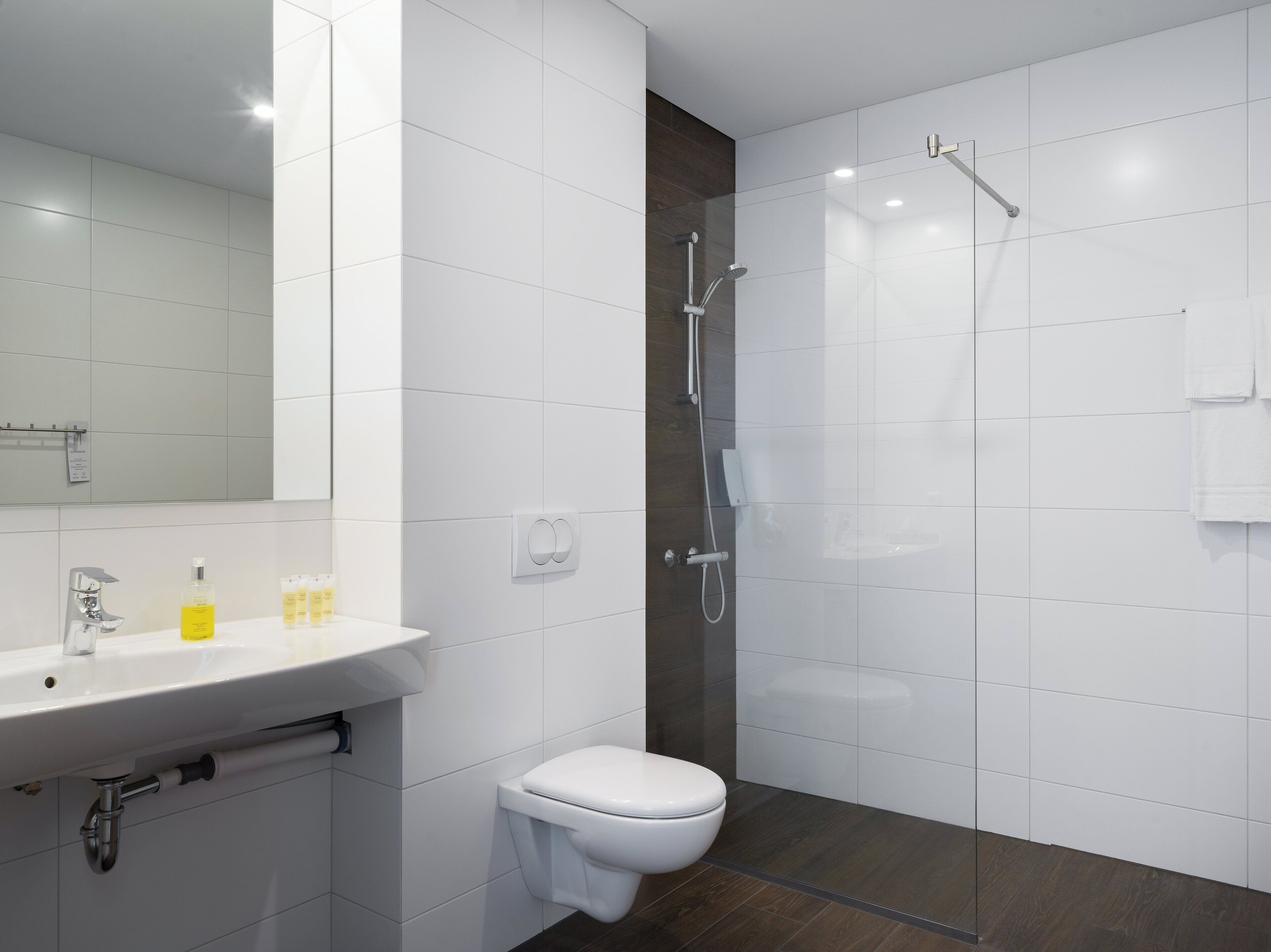 A modern bathroom with a white sink, mirror, and toilet, and a glass-enclosed shower area.
