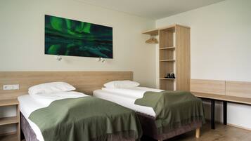 Hotelkamer met twee bedden, een houten hoofdeinde, een groene deken, een houten bureau en een schilderij van het noorderlicht.