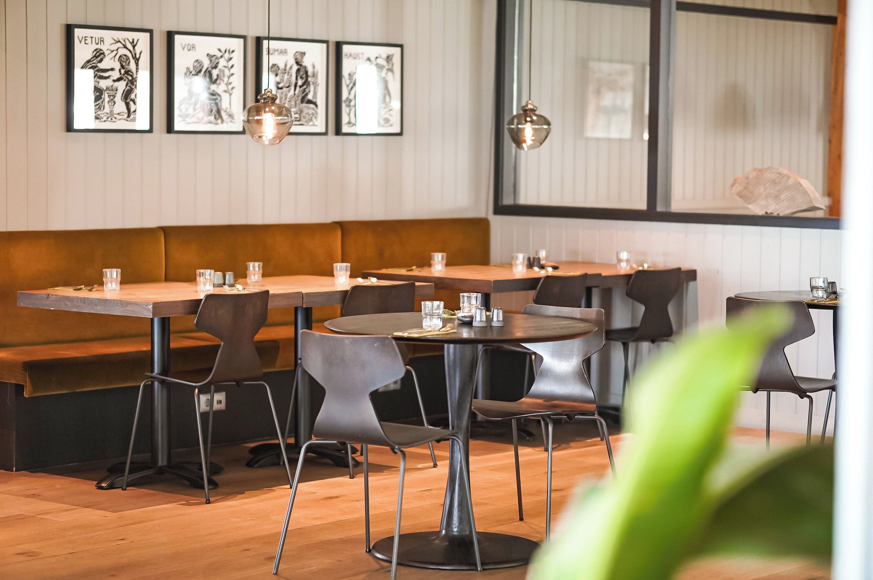 Un restaurante con mesas y sillas de madera, obras de arte enmarcadas en la pared y un ventanal grande.