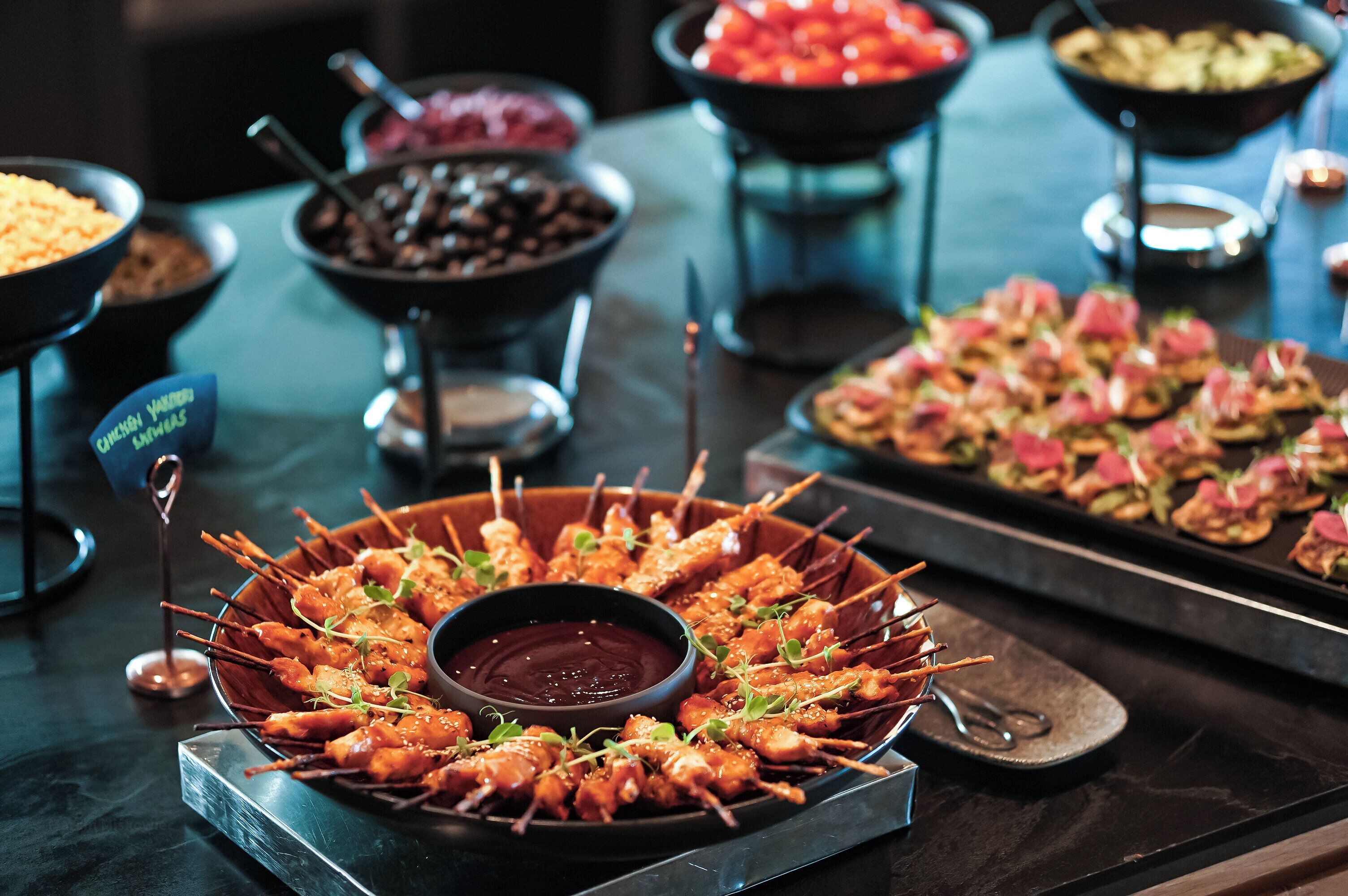 Una mesa de buffet con diversos alimentos, incluyendo brochetas, salsas y aperitivos.