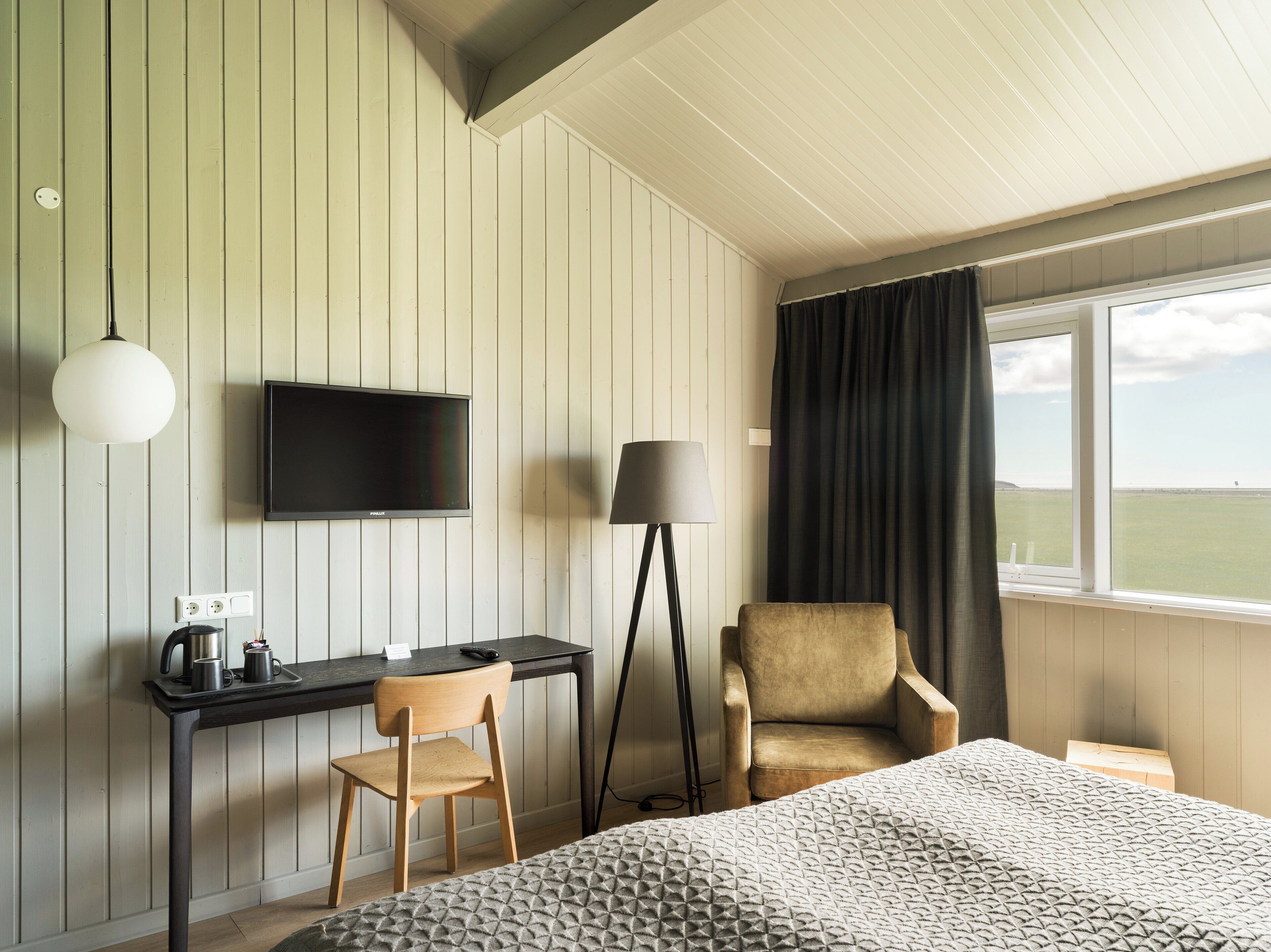 A hotel room with a bed, a desk with a chair, a TV, a lamp, and a view of the outdoors.