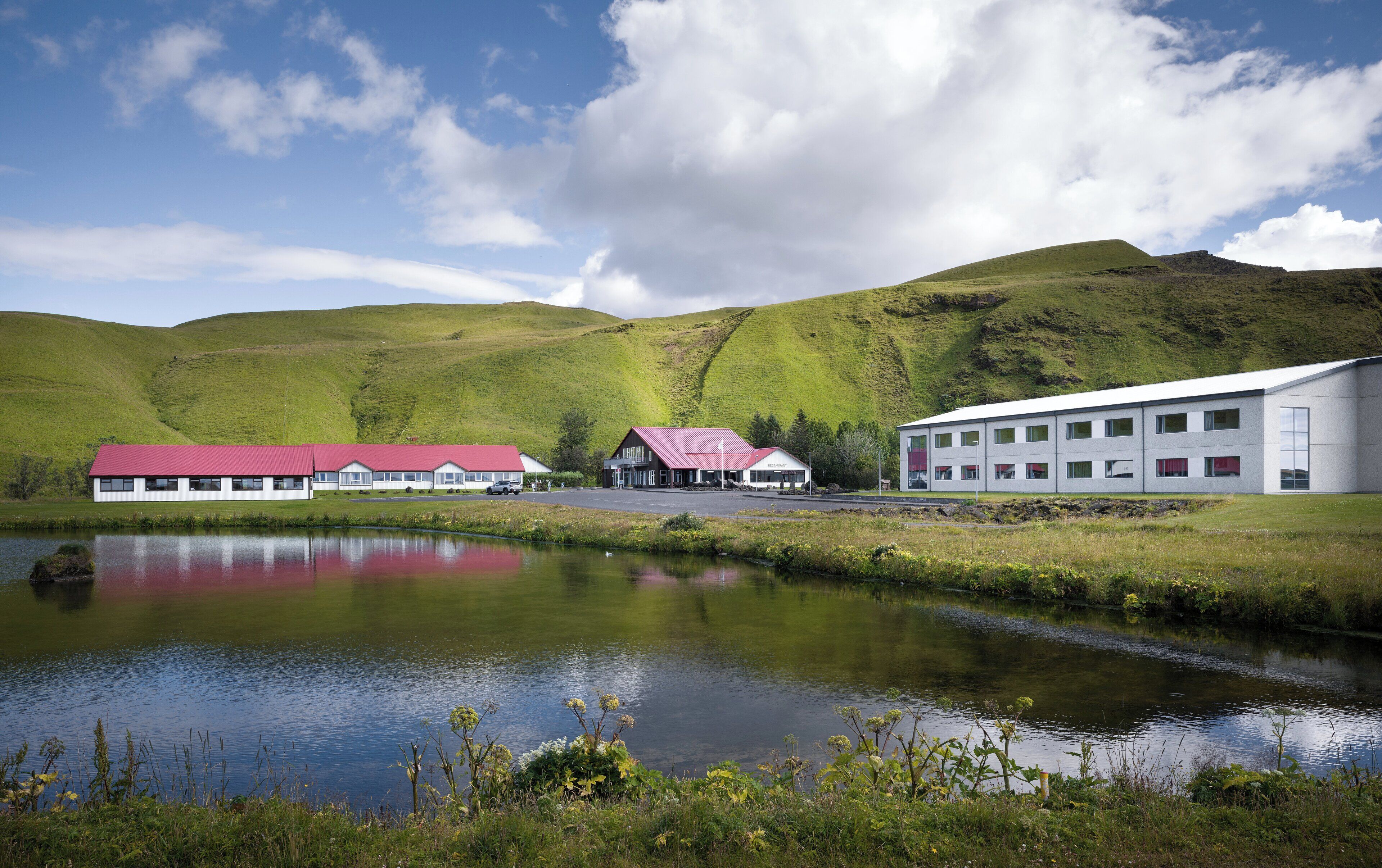 A modern building with a red roof and a white facade, situated beside a calm lake with a reflection.