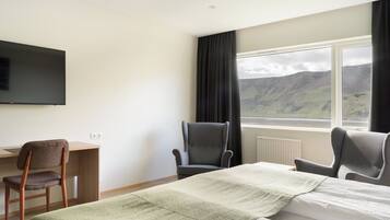 Une chambre d’hôtel comprenant un lit, deux chaises, un bureau, une télévision et une fenêtre donnant sur un paysage montagneux.
