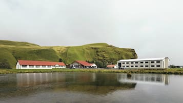A lakeside building with a red roof, surrounded by green hills.