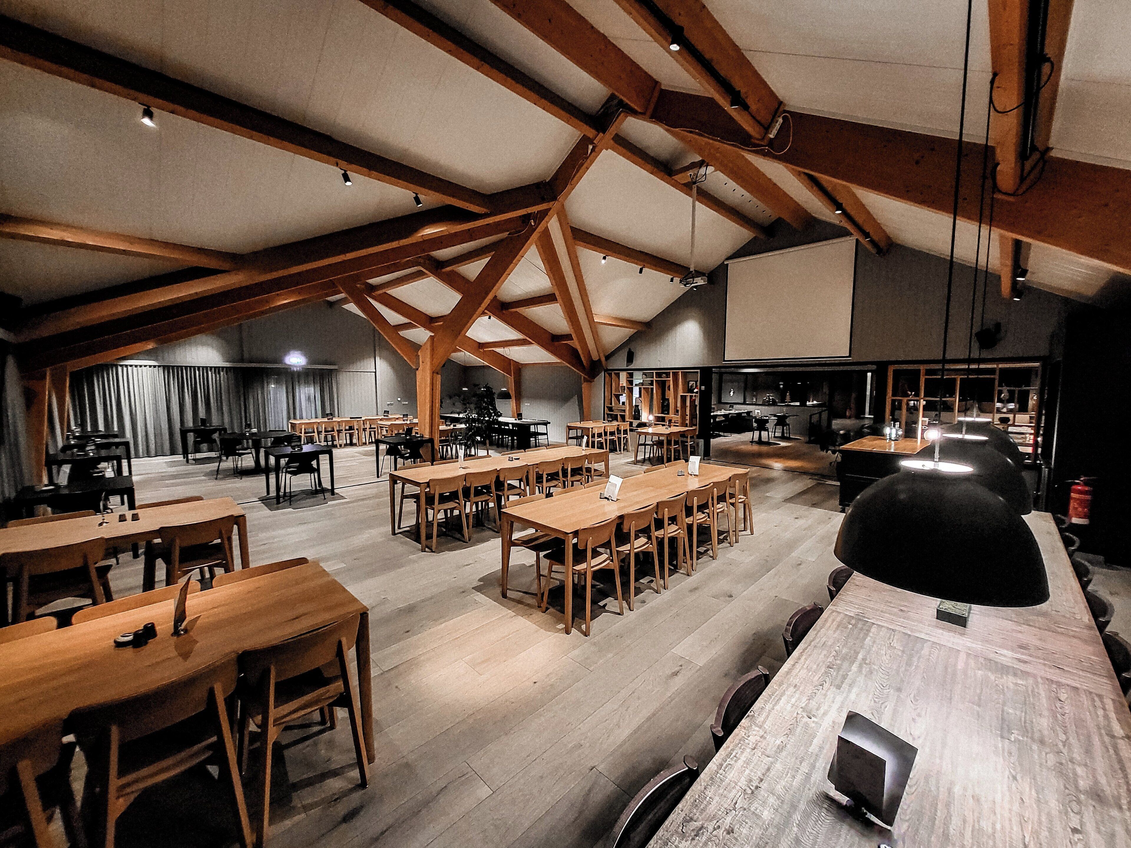 Un comedor espacioso con techos altos y vigas de madera a la vista, con varias mesas y sillas.