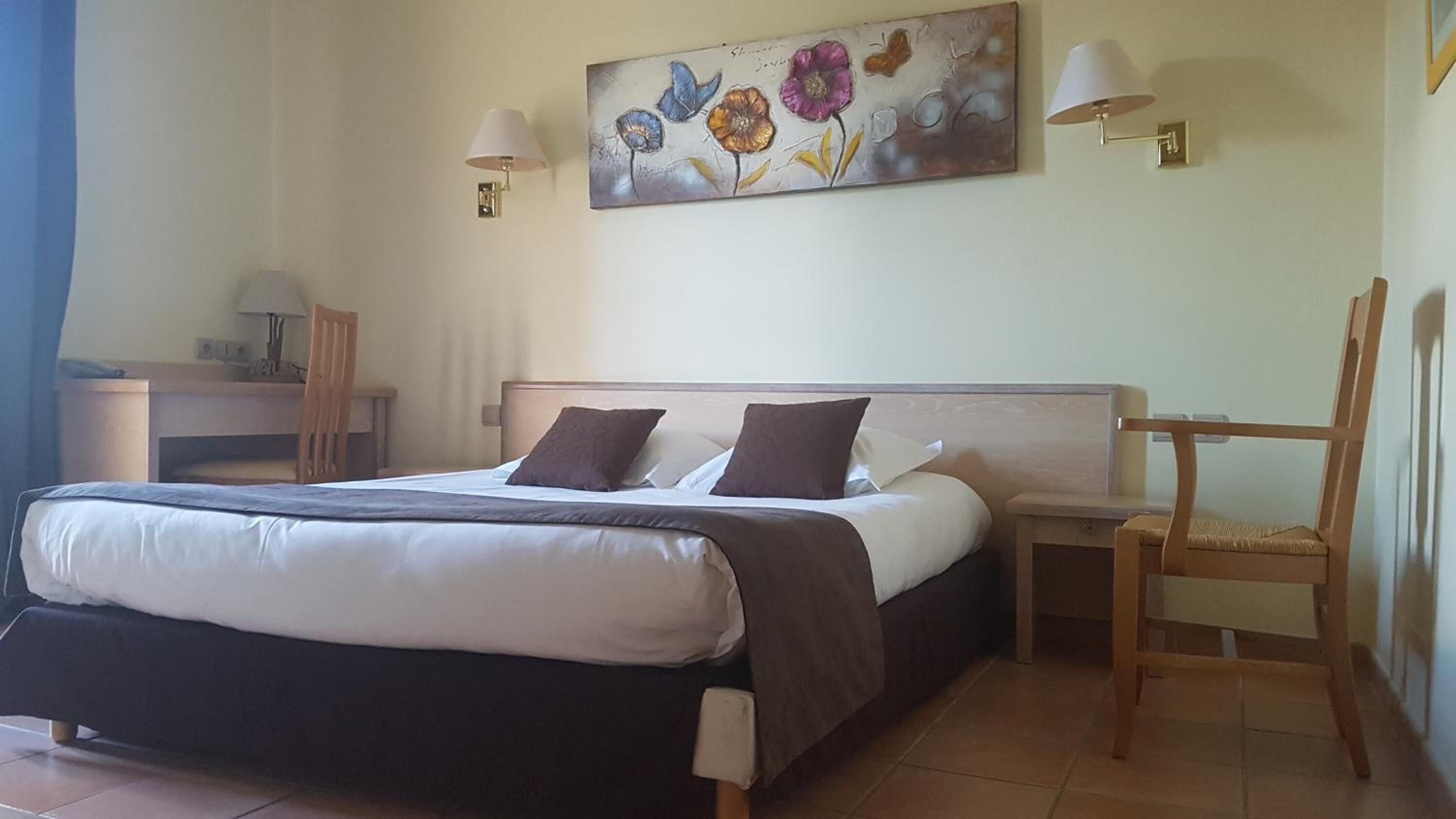 A hotel room with a bed, bedside tables, a desk, and a chair.