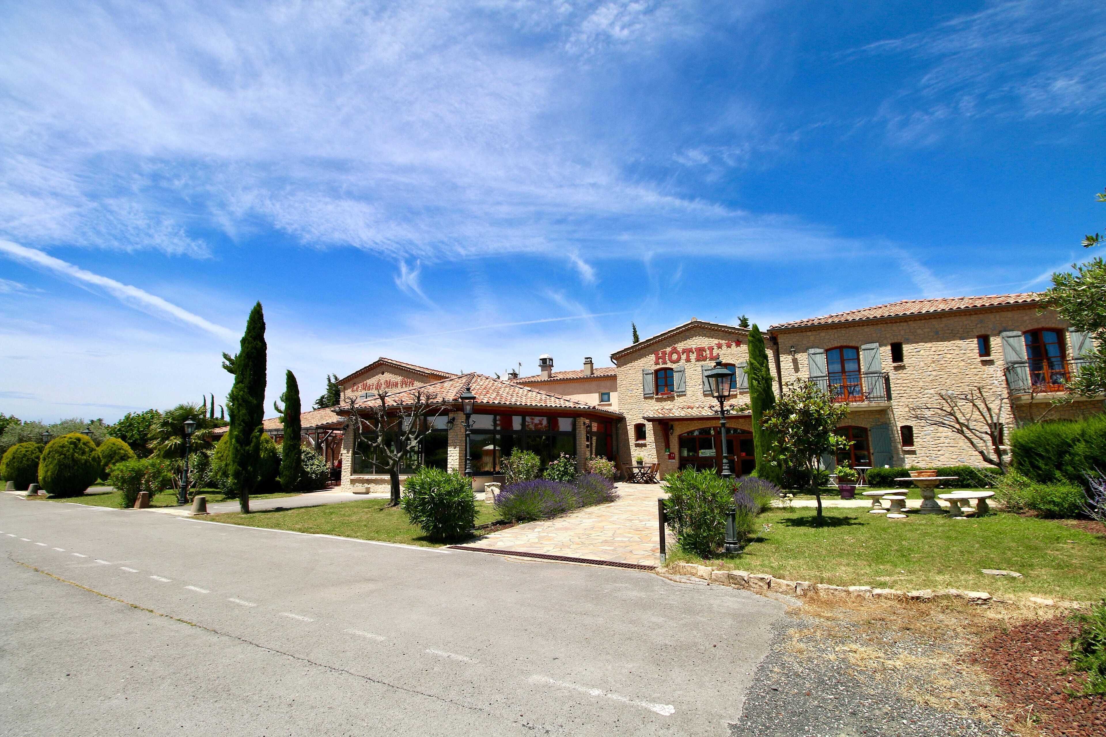 A hotel with a stone facade, a tiled roof, and a well-maintained lawn.