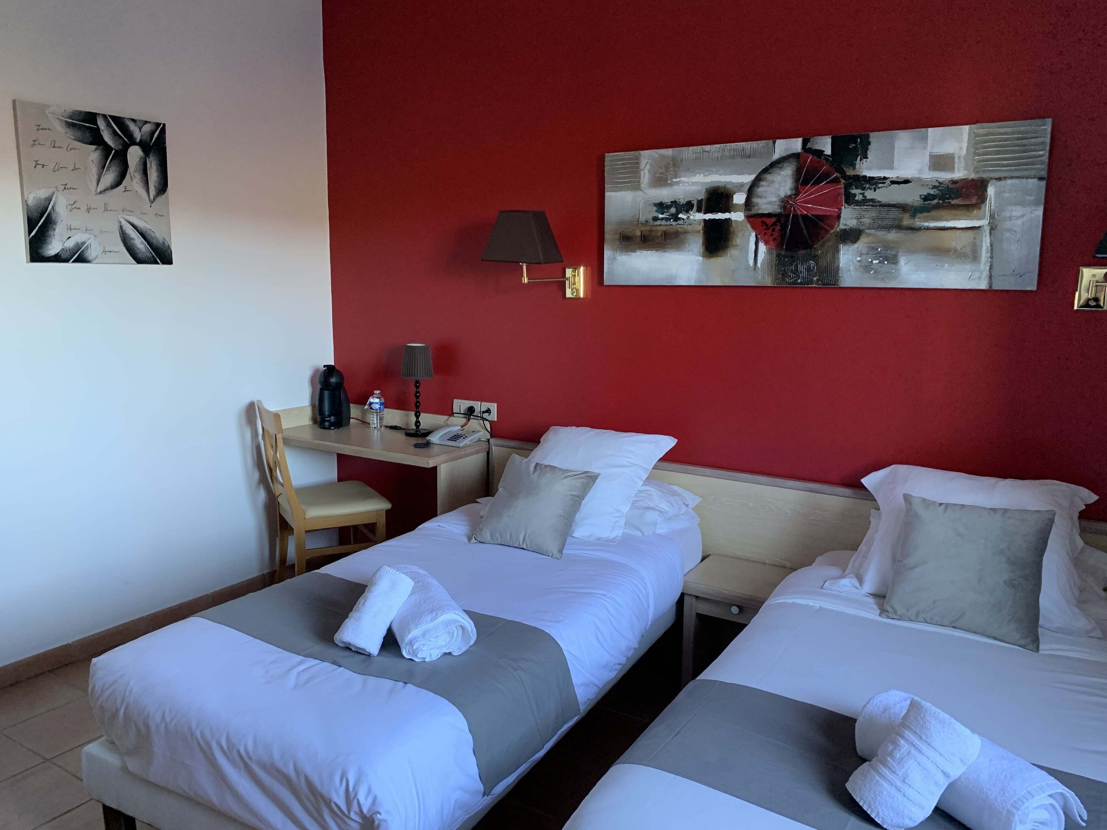 A hotel room with two beds, a desk, a chair, a lamp, and artwork on the walls.