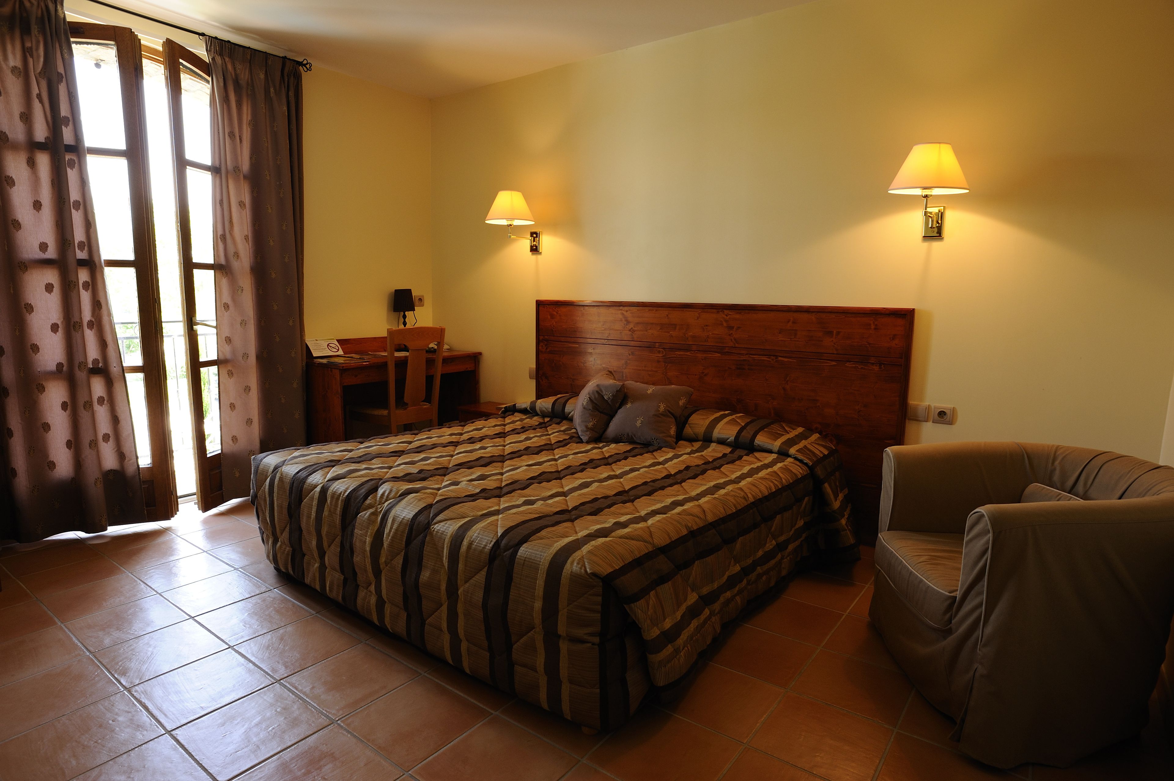 Een hotelkamer met een groot bed, twee bedlampen, een houten hoofdbord, een stoel en een bureau met een stoel.