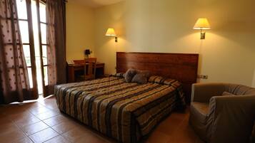Habitación de hotel con una cama grande, dos lámparas de noche, un cabecero de madera, una silla y un escritorio con su correspondiente silla.