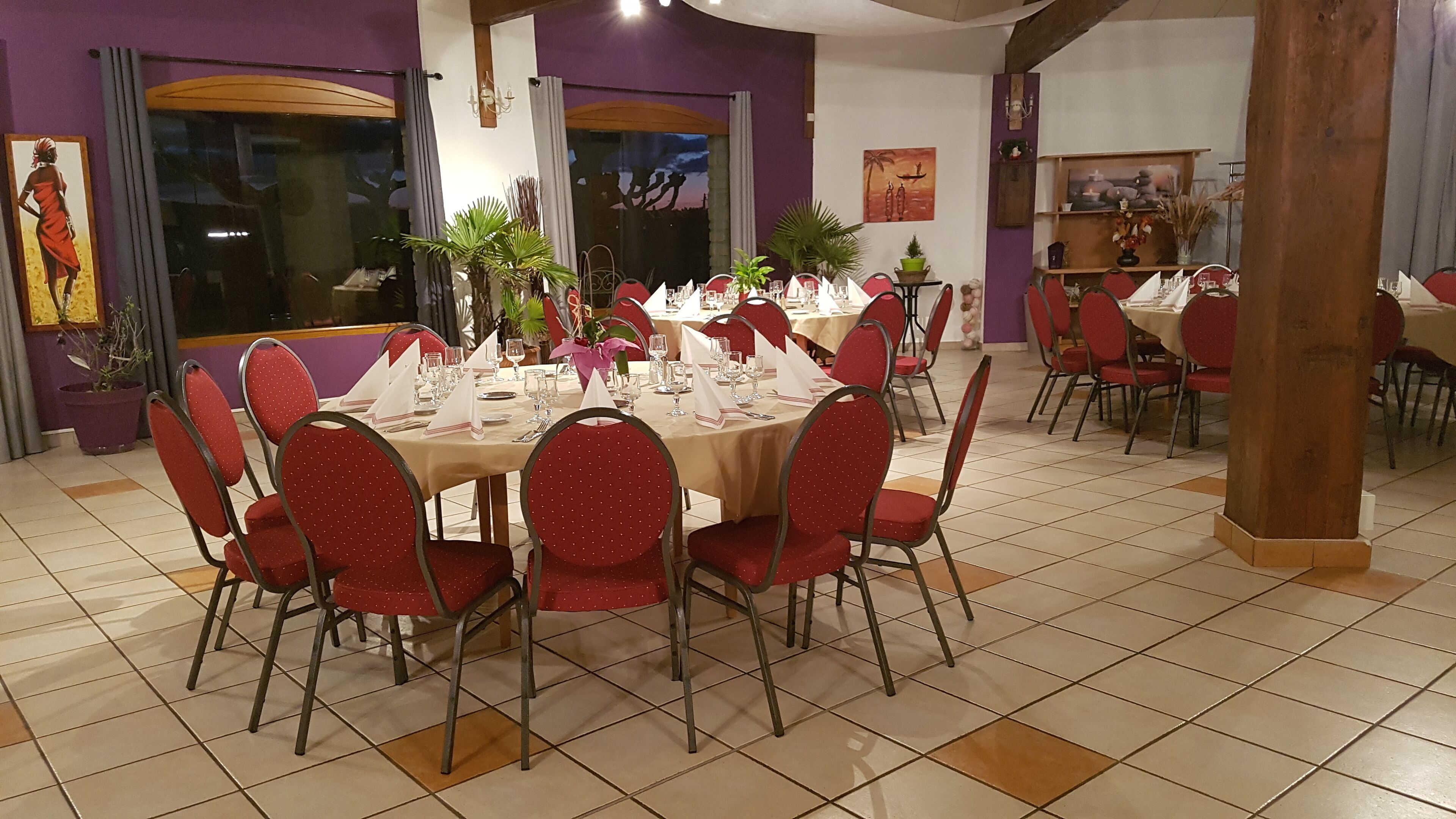 A dining area with round tables set for multiple guests, red chairs, and various table settings.