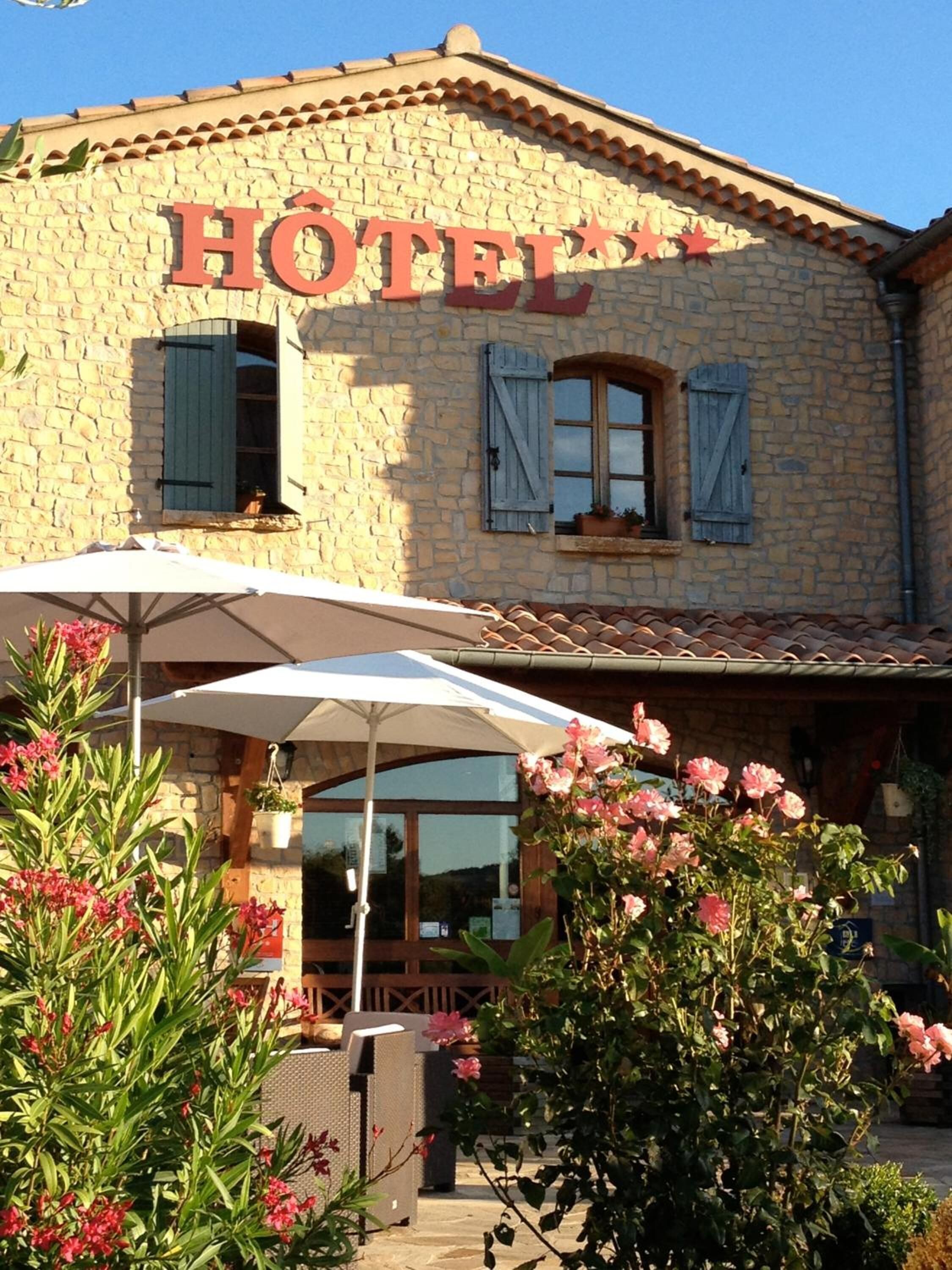 A stone building with a sign reading "HOTEL" and a patio area with outdoor furniture and umbrellas.