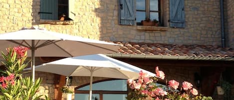 A stone building with a sign reading "HOTEL" and a patio area with outdoor furniture and umbrellas.