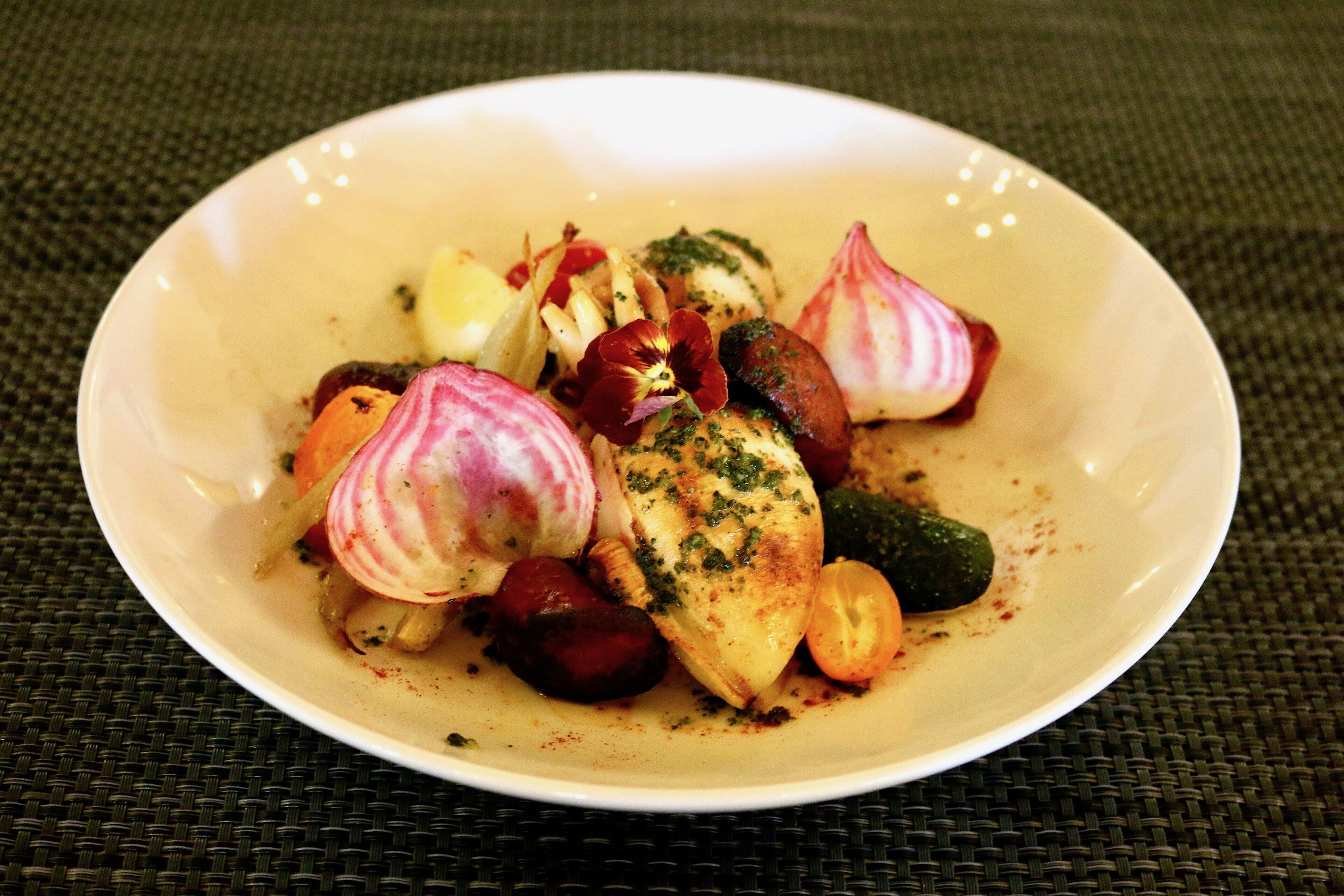 A white plate with a variety of vegetables and a piece of chicken, garnished with herbs.