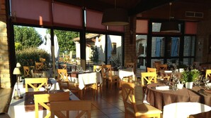 Un espacio de comedor al aire libre con varias mesas y sillas, ventanas amplias y vistas de la vegetación circundante.