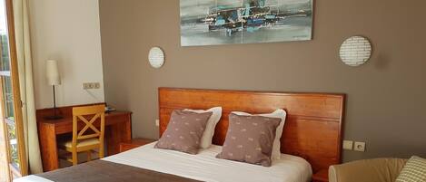 Habitación de hotel con cama de madera, dos almohadas, escritorio, silla, lámpara y un cuadro en la pared.