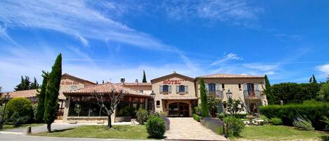 A two-story hotel with a tiled roof, a central entrance, and a well-maintained garden.