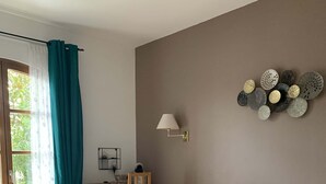 Un dormitorio ordenado con una cama grande, un escritorio con silla, una lámpara de pared y un adorno decorativo en la pared.