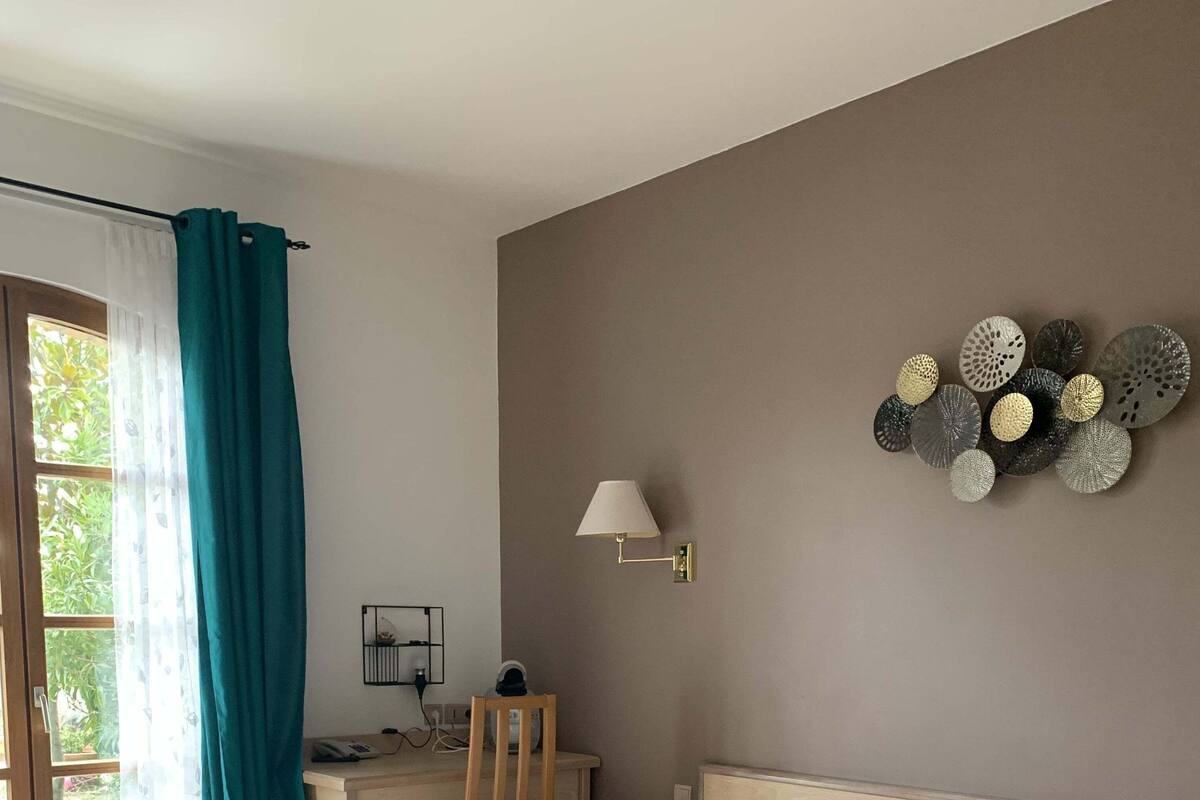 A neatly arranged bedroom with a large bed, a desk with a chair, a wall-mounted lamp, and a decorative wall piece.