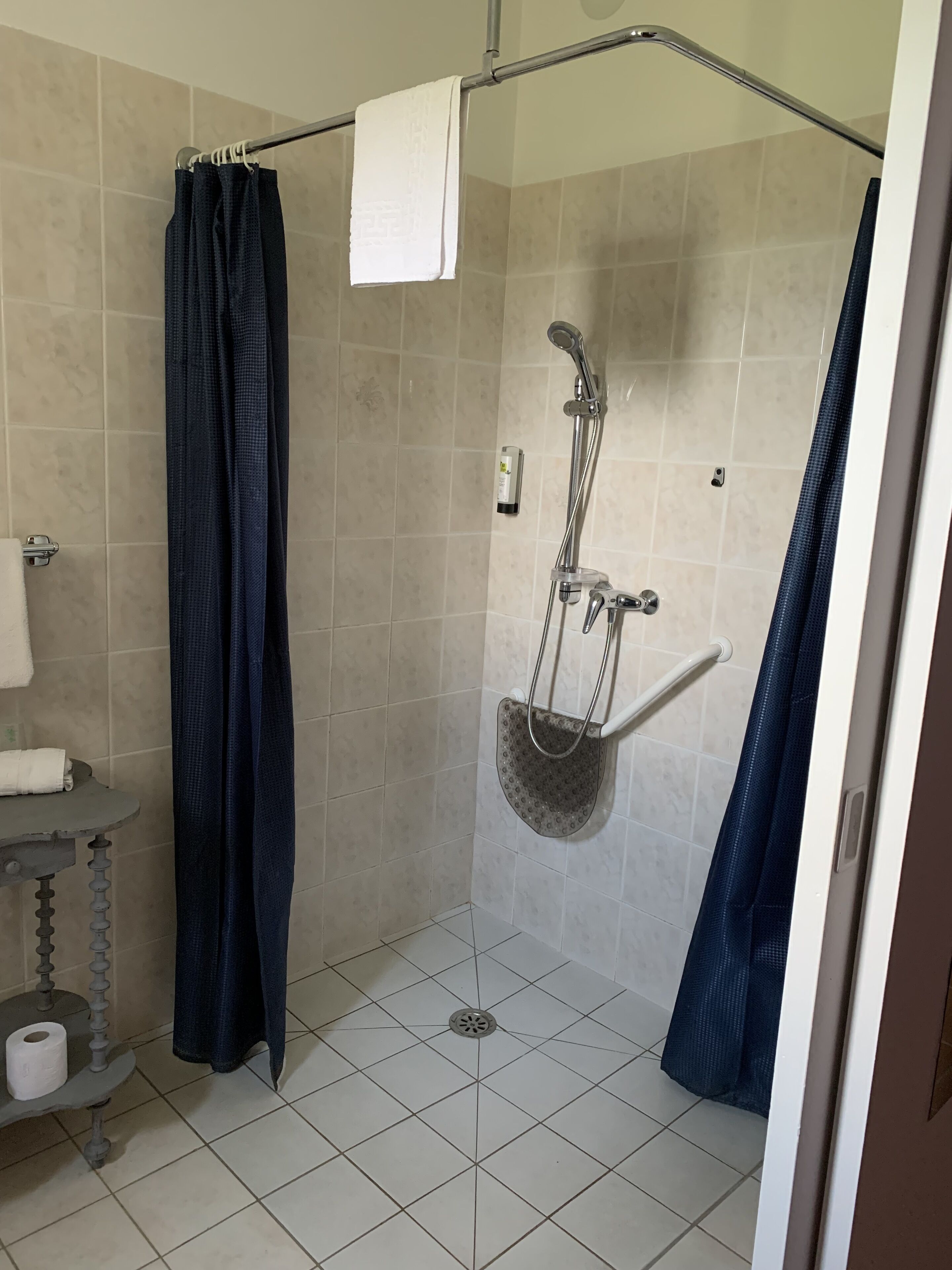 A shower area with a glass door, a towel rack, and a small shelf with toiletries.