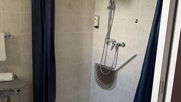 A shower area with a glass door, a towel rack, and a small shelf with toiletries.