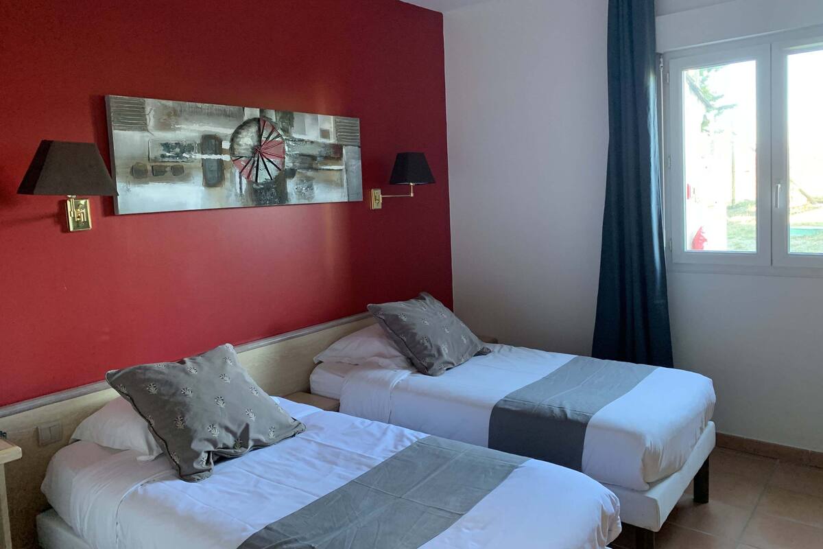 A hotel room with two beds, red walls, and a large window with curtains.