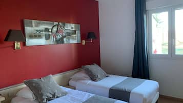 Une chambre d’hôtel avec deux lits, des murs rouges et une grande fenêtre avec des rideaux.