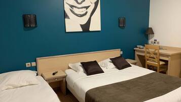 Une chambre d’hôtel avec deux lits, un bureau et une chaise. Il y a un tableau au mur et une lampe sur le bureau.