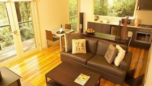 A living room with a sofa, coffee table, and a dining area with a table and chairs. There is a kitchen area with a stove and cabinets.