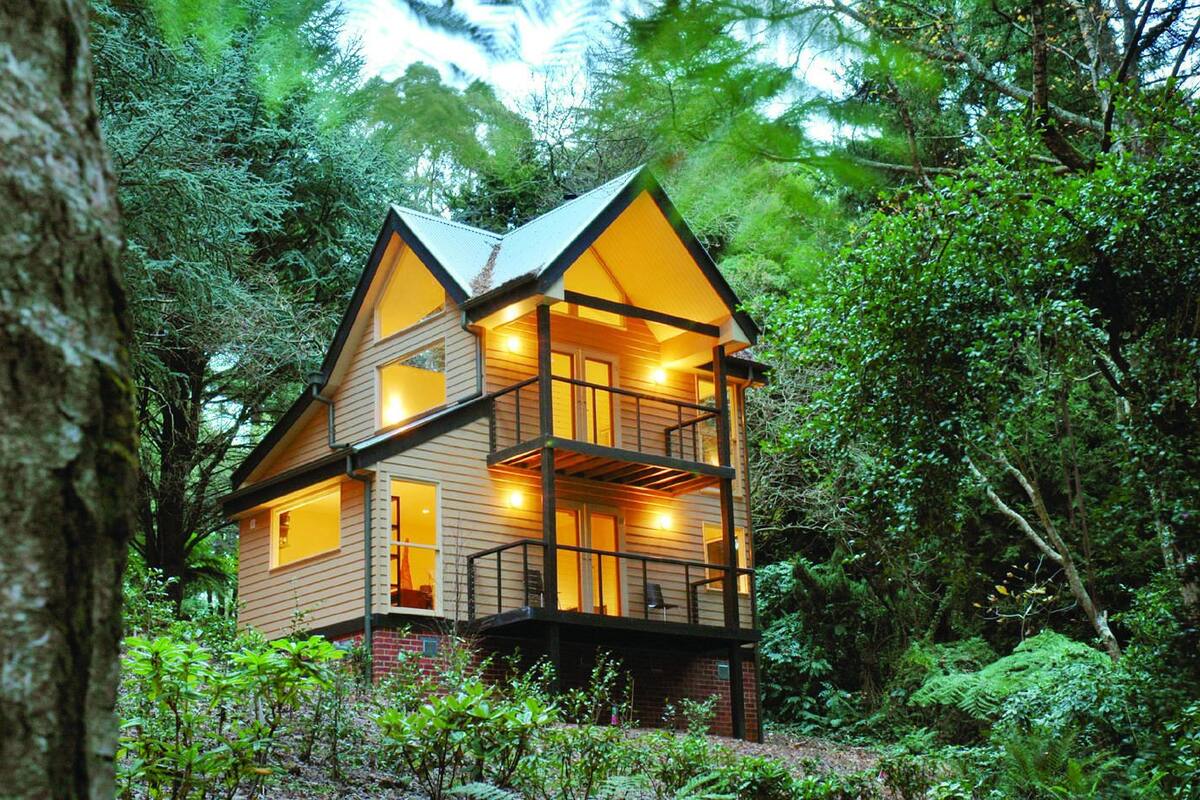 A two-story wooden cabin with a balcony, surrounded by dense forest.