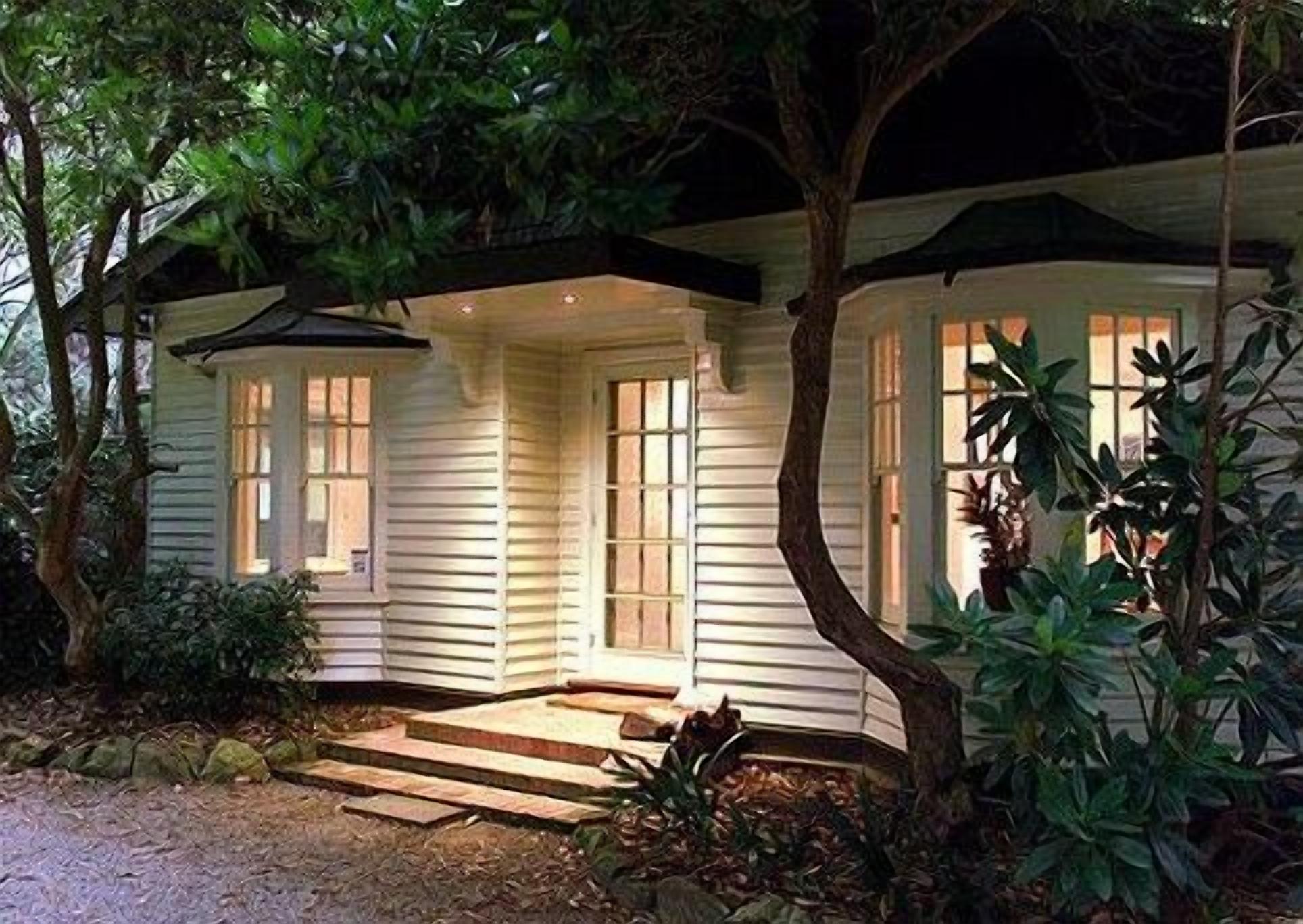 A house with a covered porch, wooden steps leading to the entrance, and a garden with various plants.