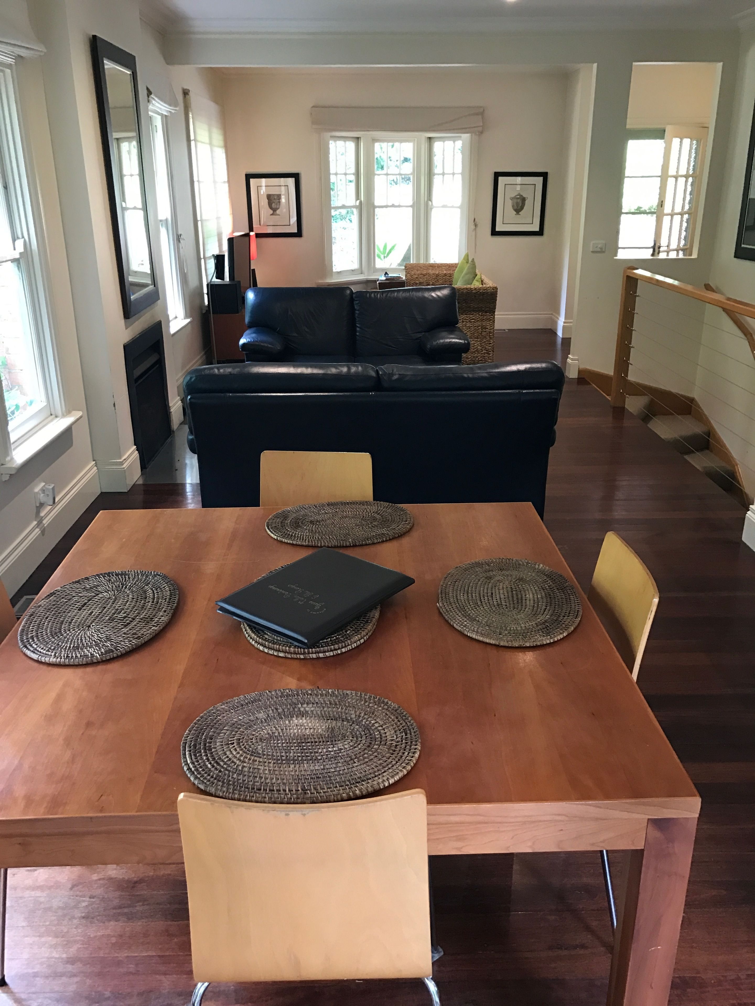 A dining area with a wooden table, four woven placemats, a laptop, and two chairs.