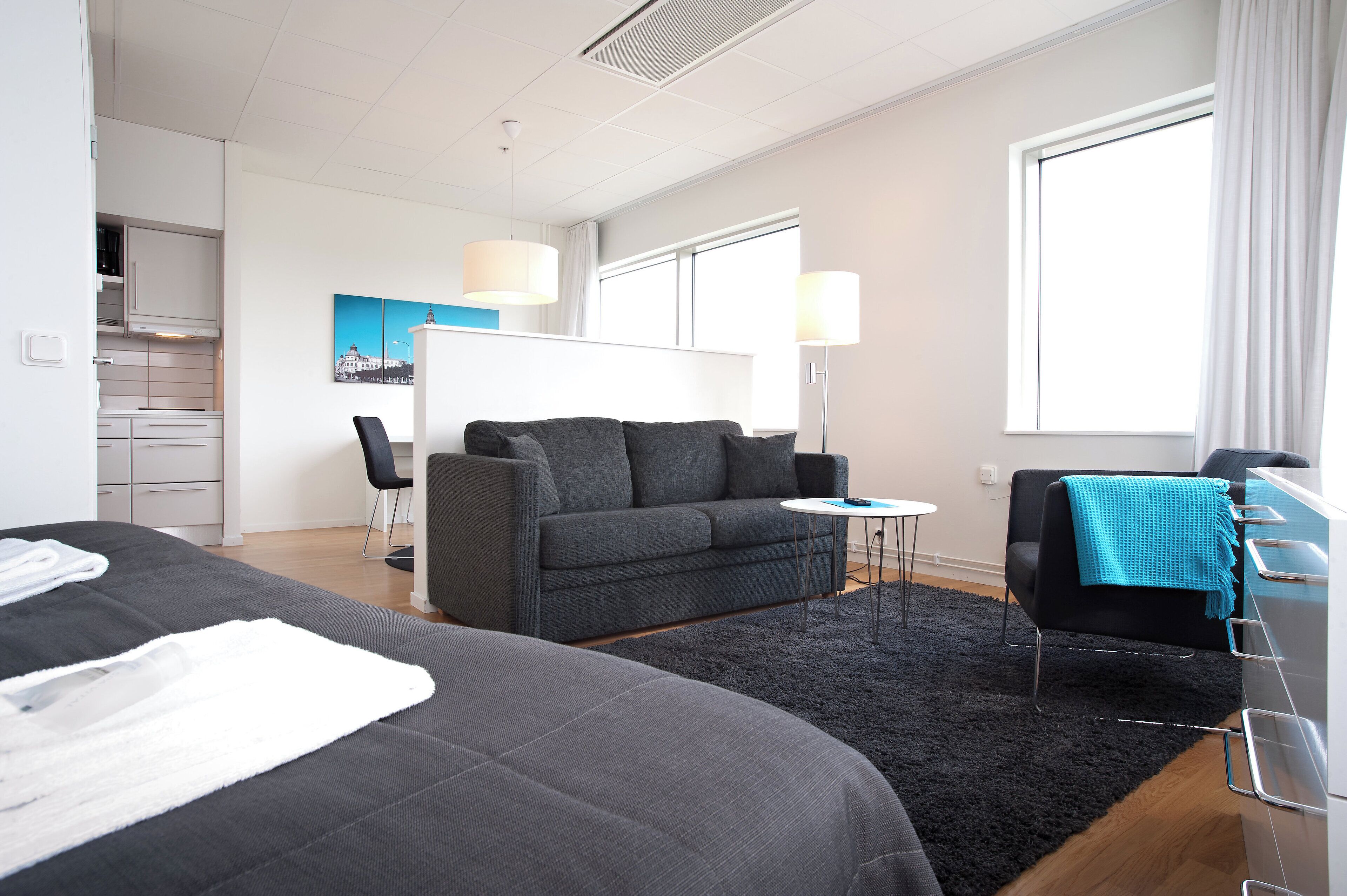 A hotel room with a bed, a sofa, a small table, a chair, a desk, and a window.