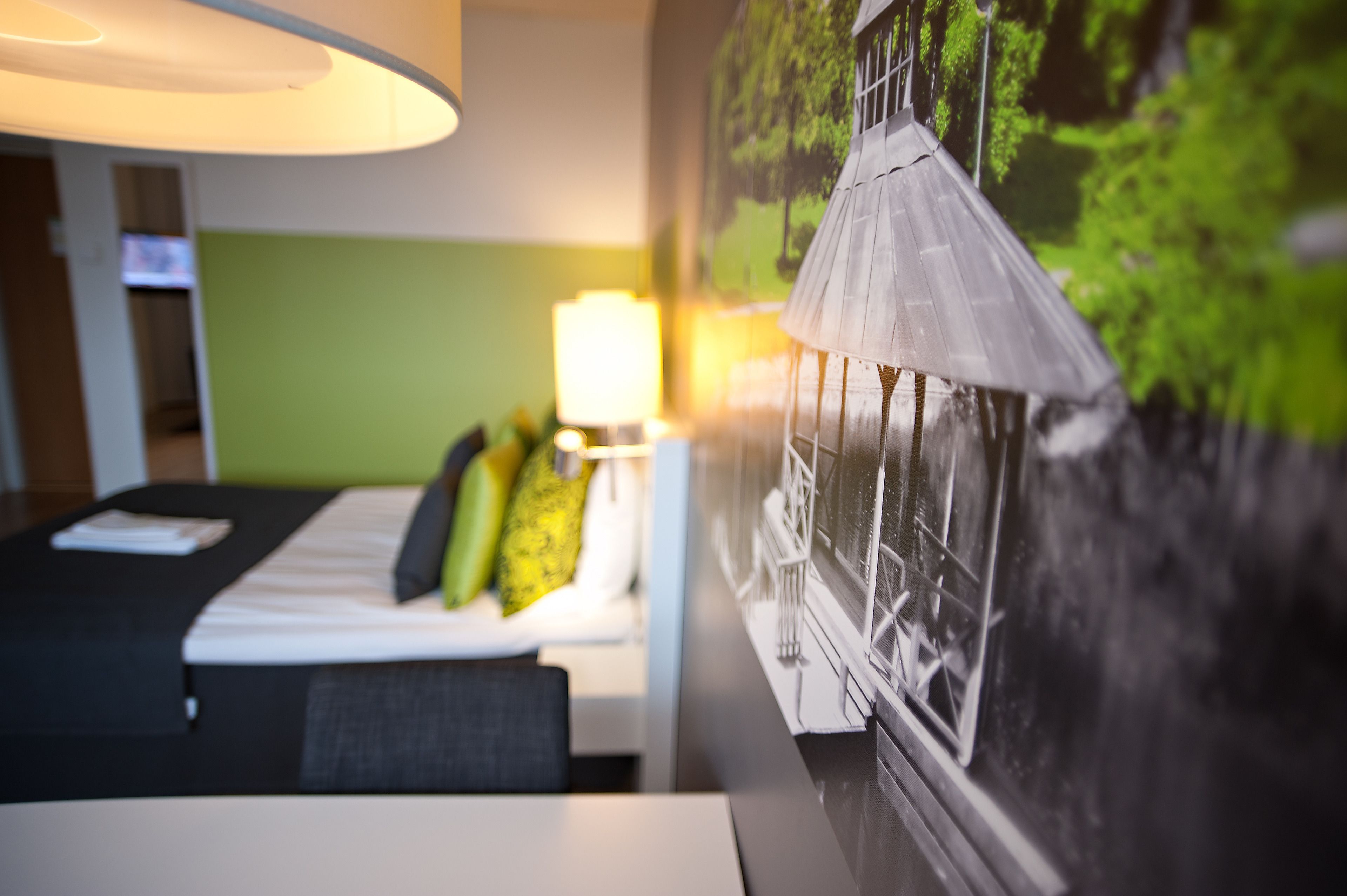 Una habitación de hotel con cama, escritorio, lámpara y un mural en la pared.