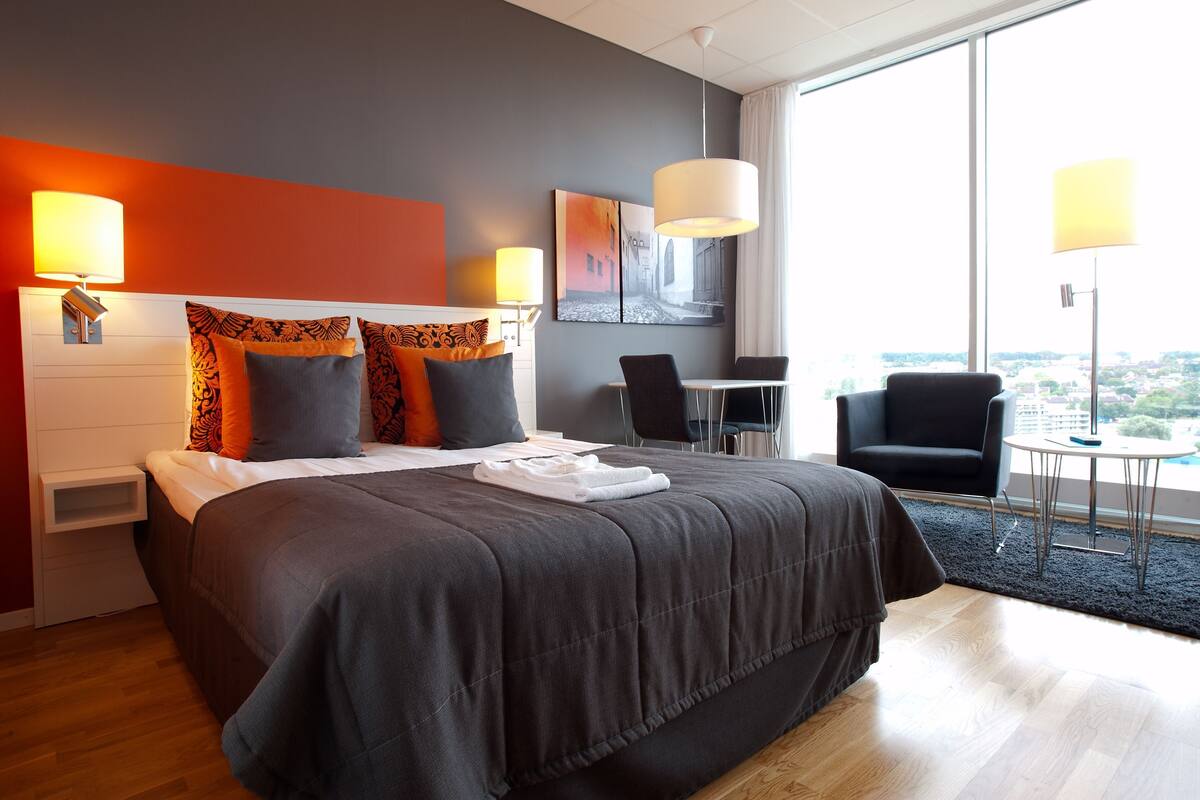A modern hotel room with a large bed, a desk, and a chair.