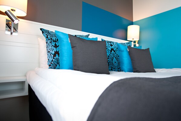 Una cama bien hecha con ropa de cama blanca y gris, almohadas estampadas en azul y un cabecero moderno.