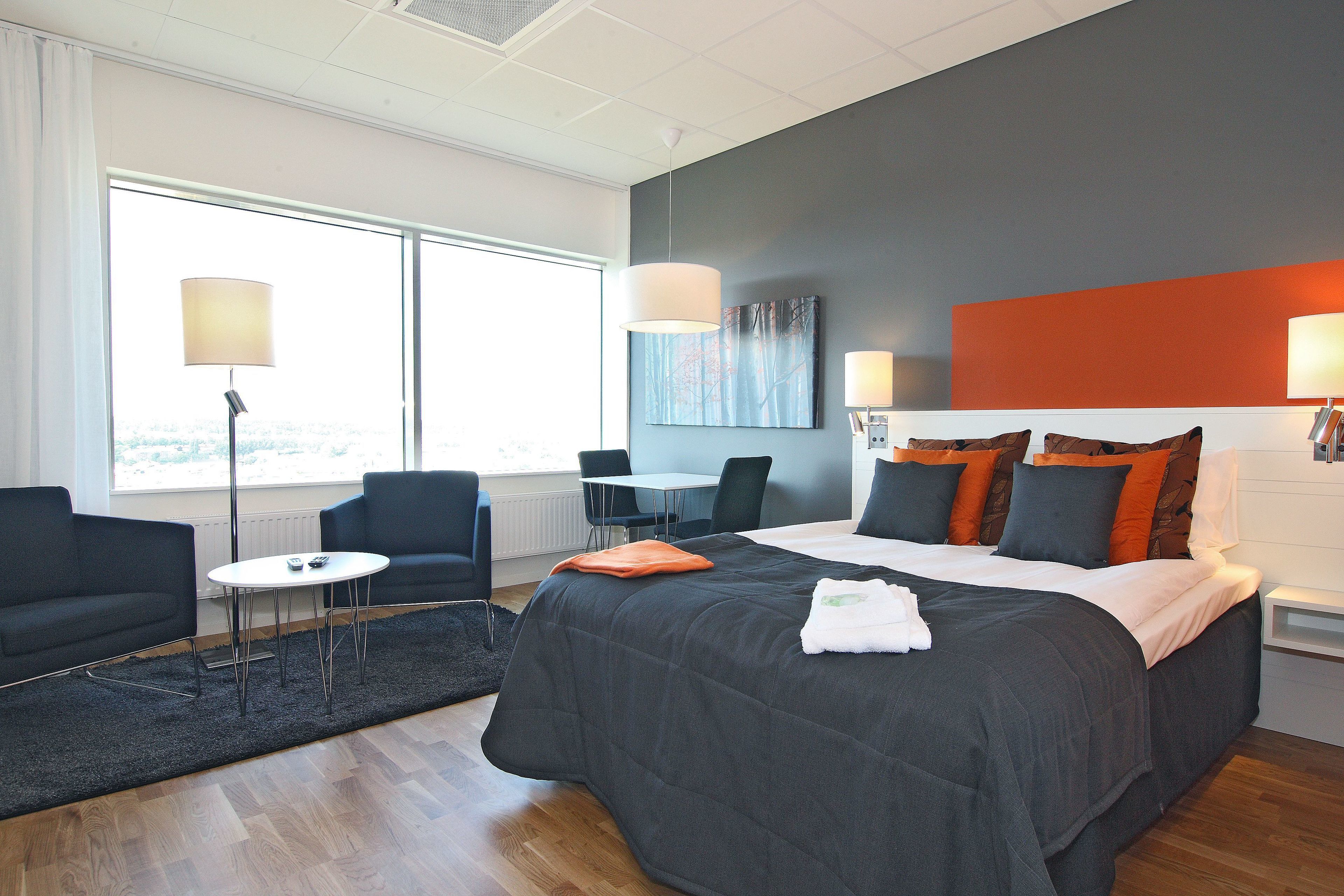 Ett hotellrum med en stor säng, ett skrivbord och en stol. Det finns ett fönster som släpper in naturligt ljus och erbjuder utsikt över omgivningarna.