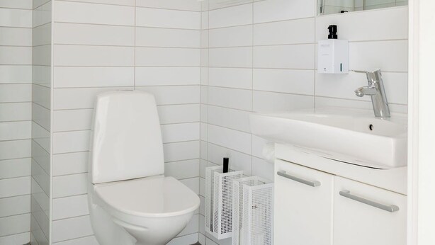 A modern bathroom with a white toilet, a white sink, and a mirror. - Sky Hotel Apartments Tornet (Linkoping)