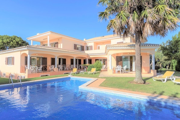 A two-story building with a swimming pool, outdoor seating, and palm trees.