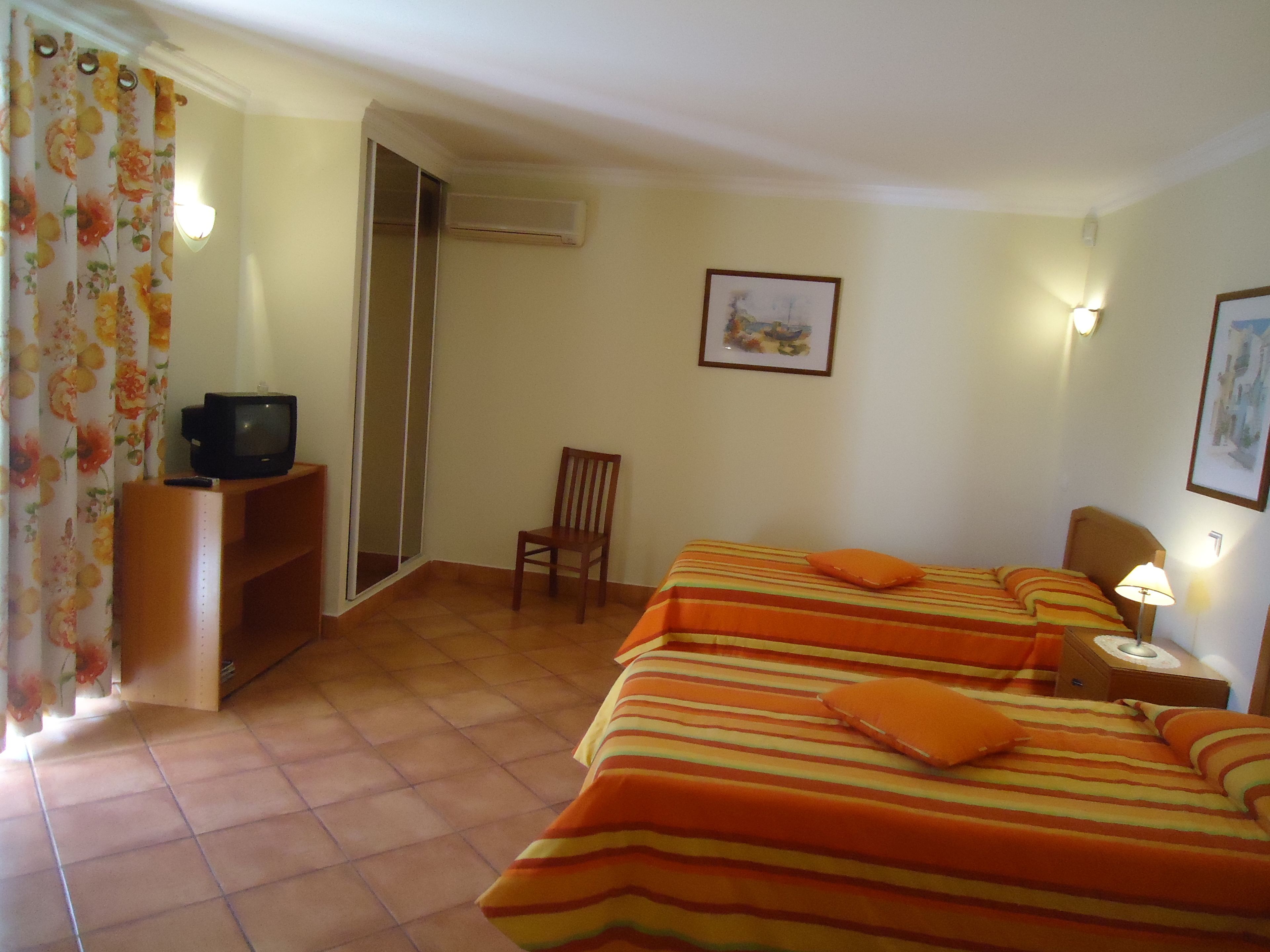 Une chambre d’hôtel avec deux lits, une chaise, un téléviseur posé sur un meuble et un espace douche.